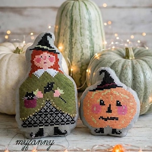 Può includere: Due ornamenti in tessuto imbottito con disegni a punto croce. Uno è una strega con capelli rossi, vestito verde e un gatto nero. L'altro è una zucca arancione rotonda con un cappello nero. Entrambi hanno il retro in tessuto grigio e stivali neri.