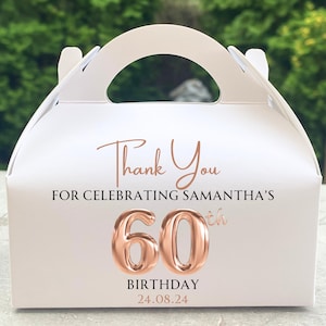 Könnte beinhalten: Weiße Geschenkbox mit Griff, verziert mit roségoldenem Text. Der Text lautet "Thank You FOR CELEBRATING SAMANTHA'S 60th BIRTHDAY 24.08.24". Die Zahl "60" ist in einer roségoldenen Metallic-Schrift.