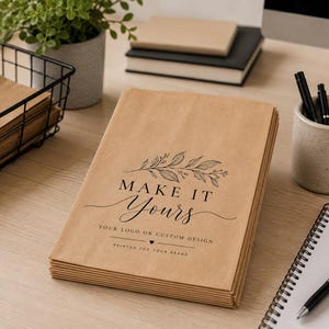 May include: A stack of light brown kraft paper bags featuring a black printed design of a leafy branch above the text "MAKE IT Yours" and "YOUR LOGO OR CUSTOM DESIGN" with a small heart icon and the phrase "PRINTED FOR YOUR BRAND" below.