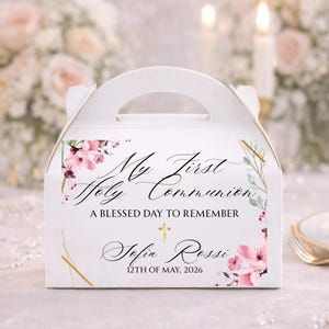 May include: White favor box with a handle, decorated with floral accents and gold lines. The box features the text "My First Holy Communion" and the name "Sofia Rossi" with the date "12th of May, 2026".