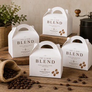 May include: Four white cardboard gable boxes with handles, each printed with the text "TRY A NEW BLEND," "FRESHLY ROASTED COFFEE," and "NORTH ROAST COFFEE CO." along with small coffee bean illustrations. Loose roasted coffee beans are scattered nearby.