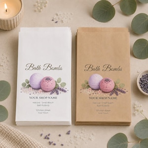 May include: Two stacks of rectangular paper bags, one white and one brown, each printed with the text Bath Bombs, YOUR SHOP NAME, Natural Small Batch Bath & Body, and 123 Main Street Your Town, featuring illustrations of bath bombs and lavender.