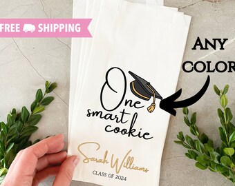 May include: White favor bag with a black and gold graduation cap illustration and the text "One smart cookie" and "Sarah Williams Class of 2024".