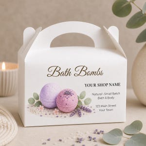 May include: A white cardboard gable box featuring the text Bath Bombs and YOUR SHOP NAME. The design includes illustrations of a light purple bath bomb, a pink bath bomb with lavender sprigs, small pink flowers, and green eucalyptus leaves.