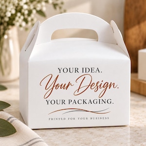 Puede incluir: Una caja de cartón blanca con asa, que presenta el texto impreso en negro y marrón: YOUR IDEA. Your Design. YOUR PACKAGING. PRINTED FOR YOUR BUSINESS, junto con dos líneas finas y curvas en marrón y negro debajo del texto.