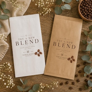 Könnte beinhalten: Zwei rechteckige Kaffeetüten aus Papier, eine weiße und eine braune, jeweils bedruckt mit dem Text TRY A NEW BLEND, FRESHLY ROASTED COFFEE, SMALL BATCH, EST 2019 und NORTH ROAST COFFEE CO, ergänzt durch eine kleine Grafik von Kaffeebohnen.