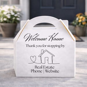 Könnte beinhalten: Eine weiße Giebelbox mit Griff, mit dem Text "Welcome Home" und "Thank you for stopping by". Darunter eine Strichzeichnung eines Hauses und eines Herzens, mit "Real Estate Phone | Website". Die Box hat goldene Akzente.