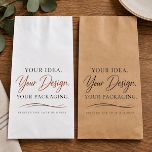 May include: Two rectangular paper bags, one white and one brown, each featuring the printed text: YOUR IDEA. Your Design. YOUR PACKAGING. PRINTED FOR YOUR BUSINESS, accompanied by two thin, curved horizontal lines below the text.