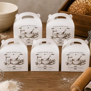 Pode incluir: Cinco caixas de cartão branco para padaria com pegas integradas, cada uma com uma ilustração impressa a preto de um saco de farinha, uma taça, um batedor e um rolo da massa, com o texto BAKED WITH LOVE e YOUR BAKERY NAME na frente.