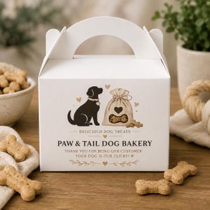 Può includere: Una scatola di cartone bianca con manico, decorata con la sagoma di un cane nero, un sacchetto di croccantini a forma di osso e il testo: DELICIOUS DOG TREATS, PAW & TAIL DOG BAKERY, THANK YOU FOR BEING OUR CUSTOMER, YOUR DOG IS OUR CLIENT!