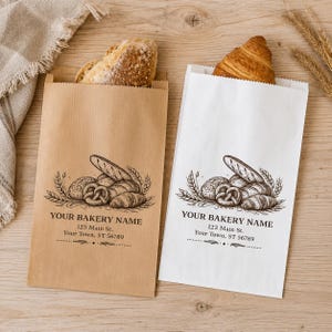 May include: Two rectangular paper bags, one brown and one white, each featuring a black ink illustration of assorted breads and the printed text YOUR BAKERY NAME, 123 Main St., Your Town, ST 56789. A loaf and a croissant protrude from the bags.
