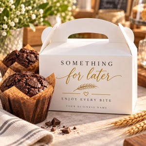 May include: A white cardboard bakery box with a handle, featuring the black and gold text "SOMETHING for later", a wheat graphic, a small heart, and the text "ENJOY EVERY BITE" and "YOUR BUSINESS NAME". Two dark chocolate muffins sit beside the box.