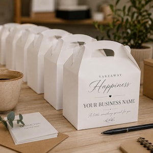 Può includere: Una fila di scatole in cartone bianco con manico, ciascuna stampata con il testo TAKEAWAY Happiness YOUR BUSINESS NAME A little something special for you. Una pila di biglietti di ringraziamento e una penna nera sono sulla superficie in legno.