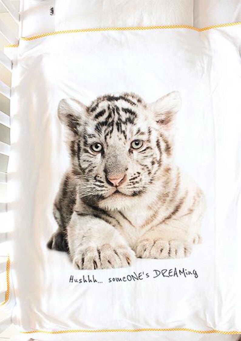 Op de afbeelding: Een wit tijgerwelpje met zwarte strepen ligt op een witte achtergrond met de tekst "Hushhh... someone's DREAMing" eronder.