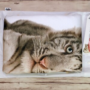 Op de afbeelding: Een witte kussensloop met een bedrukt gezicht van een witte tijgerwelp. De welp kijkt recht in de camera met zijn mond lichtjes open. De kussensloop zit in een witte envelop met een rood lint en een label met de tekst "Simones's Dream".