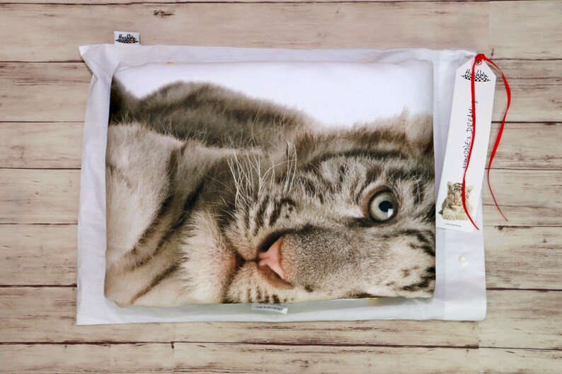 Op de afbeelding: Een witte kussensloop met een bedrukt gezicht van een witte tijgerwelp. De welp kijkt recht in de camera met zijn mond lichtjes open. De kussensloop zit in een witte envelop met een rood lint en een label met de tekst "Simones's Dream".