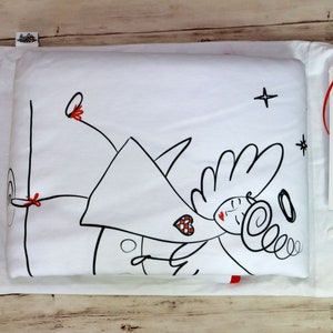 Op de afbeelding: Wit kussensloop met een zwarte en rode illustratie van een engel met vleugels, een halo en een hart. De tekst "someone is dreaming" staat op een wit label dat aan het kussensloop is bevestigd.