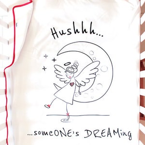 Op de afbeelding: Witte wieg lakens met een rode rand. Het laken heeft een zwart-witte illustratie van een engel met vleugels die op een halve maan staat. De tekst "Hushhh... someone's DREAMING" staat onder de illustratie.