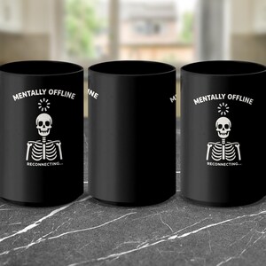Op de afbeelding: Zwarte keramische mok met een witte skeletafbeelding en de woorden "Mentally Offline, Reconnecting...". De mok heeft een groot handvat en een cilindrische vorm. Het ontwerp toont een schedel en gekruiste botten.