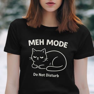 May include: Black t-shirt with the text "MEH MODE" above a white outline drawing of a cat. Below the cat is the text "Do Not Disturb". The shirt is short-sleeved.