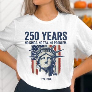 May include: White t-shirt with a graphic design commemorating 250 years. The design features the Statue of Liberty in front of a distressed American flag, with the text "250 YEARS" and the phrase "NO KINGS. NO TEA. NO PROBLEM."