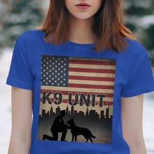May include: Royal blue t-shirt with a distressed American flag design and the text "K9 UNIT". The graphic shows a silhouette of a police officer and a dog, set against a cityscape.