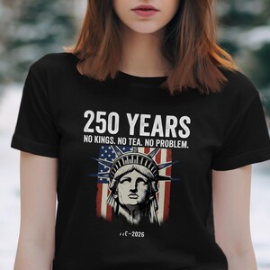 May include: Black t-shirt with a graphic of the Statue of Liberty and an American flag. The text on the shirt says "250 YEARS, NO KINGS. NO TEA. NO PROBLEM." and "...-2026".