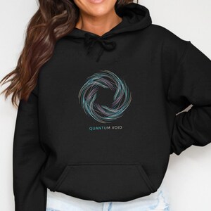 May include: Black hoodie with a circular design in shades of blue, purple, and green. The text "QUANTUM VOID" is below the design. The hoodie has a drawstring hood and a front pocket.