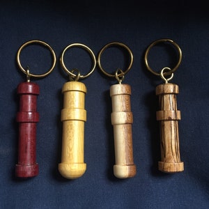 May include: Four wooden keyrings with different wood grain patterns and colours. The keyrings are attached to gold key rings. The keyrings are all about 7.5 cm long.