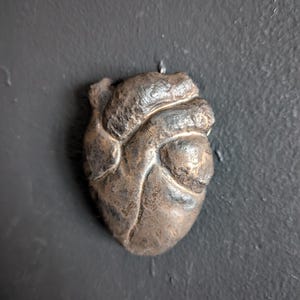 May include: A detailed, textured, metallic heart sculpture in a dark gray color.
