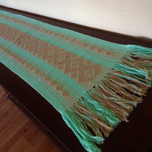 Peut inclure: Un chemin de table vert avec un motif géométrique brun et des franges aux extrémités.