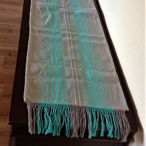 Peut inclure: Un chemin de table rayé turquoise et gris avec des franges. Le chemin de table est sur une table brun foncé.