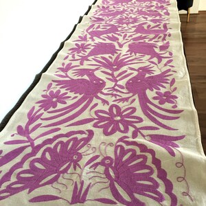 Puede incluir: Un camino de mesa de lino blanco con un diseño bordado en rosa que presenta pájaros, flores y mariposas.