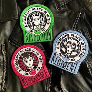 以下が含まれることがあります： 白い背景と黒い文字で刺繍された3つのパッチ。各パッチには女性の顔と「A Woman's Place Is In The」というテキストが書かれており、その後に異なる単語が続きます。最初のパッチは緑色で「Revolution」と書いてあります。2番目のパッチは青色で「Regiment」と書いてあります。3番目のパッチはピンク色で「Renaissance」と書いてあります。