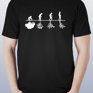 以下が含まれることがあります： 人類の進化を描いた白いグラフィックが特徴の黒いTシャツ。デザインは、霊長類のような姿から現代人へと進化する様子を表現しており、各人物の下には根が描かれています。Tシャツはクルーネックで半袖です。