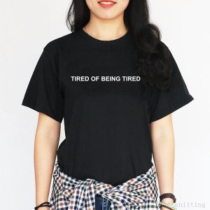 May include: Black t-shirt with white text that reads "TIRED OF BEING TIRED".