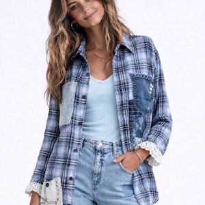 May include: Blue plaid shirt with denim patches and lace trim. The shirt has a button-down front and long sleeves. The model is wearing a light blue tank top and light wash jeans.
