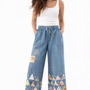 May include: Light blue denim culottes with a drawstring waist and patch pockets. The pants feature colorful patchwork triangles along the hem and a floral patch on the front. A white tank top completes the outfit.