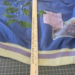 Puede incluir: Una sudadera azul con cuello redondo y dobladillo acanalado. La sudadera presenta un dise&ntilde;o floral con bayas azules y hojas verdes. Tiene un bolsillo y ribete de color lila claro. La longitud de la sudadera es de aproximadamente 63.5 cm.