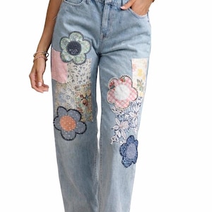 May include: Light blue denim jeans with colorful floral patches. The patches are in various shapes and sizes, with different patterns and colors, including pink, blue, and white. The jeans have a classic five-pocket design.