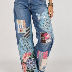 May include: Blue denim jeans featuring a patchwork design with various fabric patterns including light blue paisley, floral rose prints, striped fabric, polka dots, and a butterfly graphic. The jeans include a small rectangular label with the word Love.