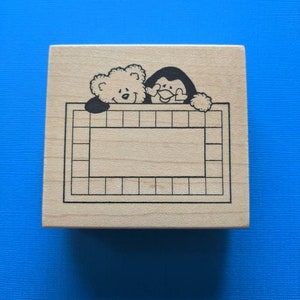 May include: Wooden stamp with a bear and penguin peeking over a gridded frame. The frame is blank and ready for personalization.