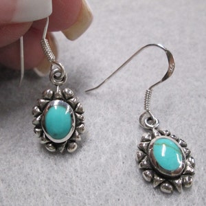 May include: A pair of silver dangle earrings with turquoise stones set in a silver flower design.