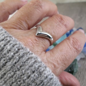 May include: A silver V-shaped ring on a hand wearing a gray knitted sweater.