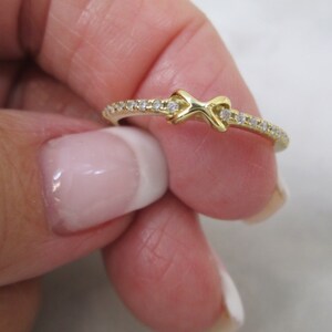 May include: A gold ring with a knot design and a row of small diamonds around the band.