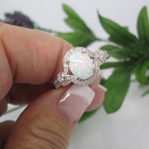 May include: A silver ring with a white opal gemstone surrounded by smaller clear gemstones. The ring has a twisted band.