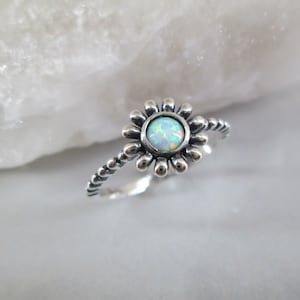 May include: A silver ring with a white opal gemstone set in a flower design. The band is twisted and has a beaded texture.