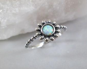 May include: A silver ring with a white opal gemstone set in a flower design. The band is twisted and has a beaded texture.