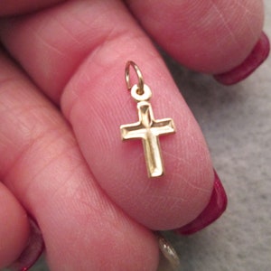 May include: A small gold cross charm pendant. The cross is detailed with a diamond-shaped pattern.
