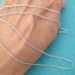 May include: A silver chain necklace, shown laid out on a person's wrist. The chain is a simple curb style.